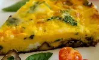 A slice of frittata with spinach and mushrooms on a white plate, garnished with cherry tomatoes and a fresh basil leaf, conveying a fresh, appetizing look.