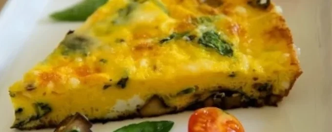 A slice of frittata with spinach and mushrooms on a white plate, garnished with cherry tomatoes and a fresh basil leaf, conveying a fresh, appetizing look.